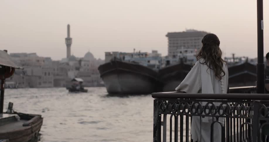 Woman wearing white dress looks out at some boats