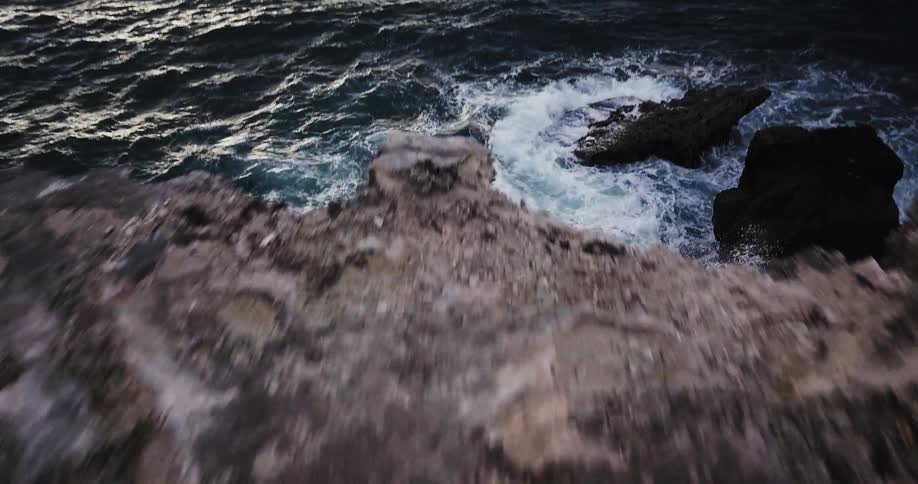 Ocean waves break against the rocks at the bottom of the cliff