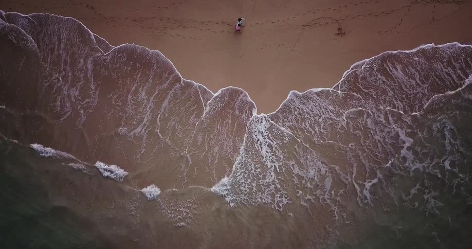 An overhead view of people walking on the beach with the water coming in