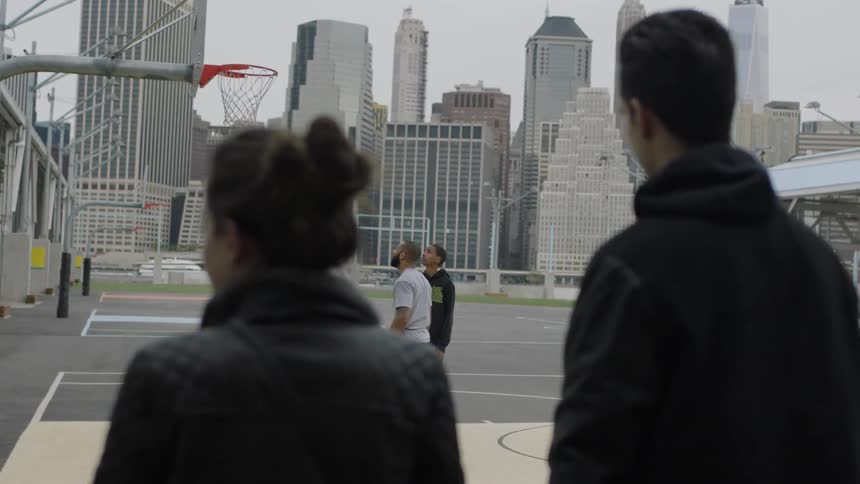 People watch men play basketball on an outside city court