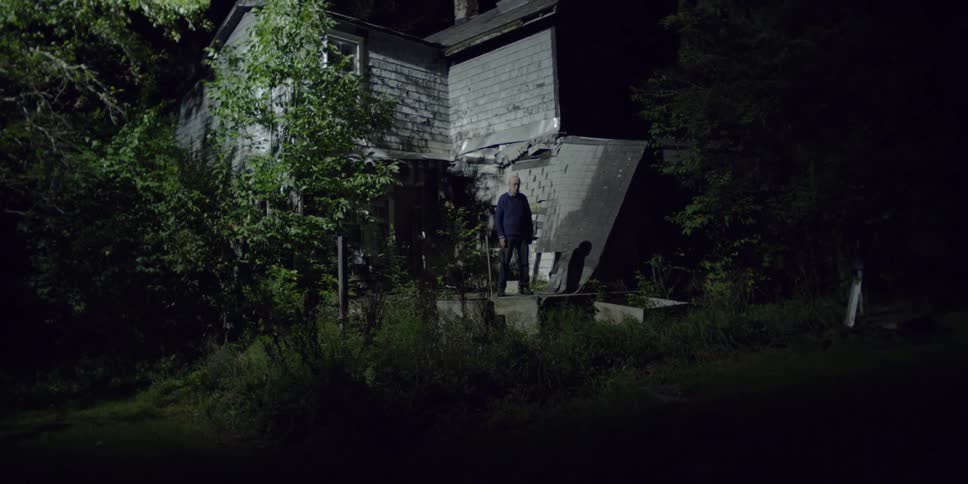 A man stands on the porch of a damaged house