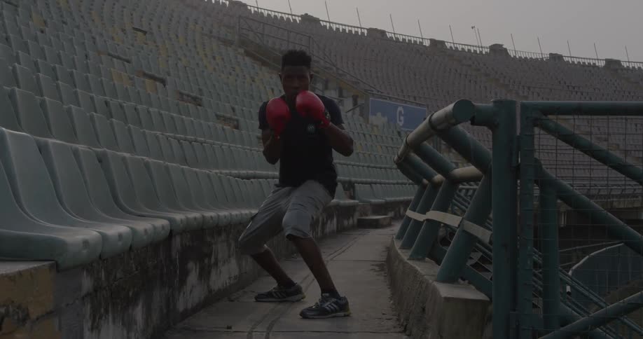 A male athlete is shadow boxing in the stands of a stadium during the day