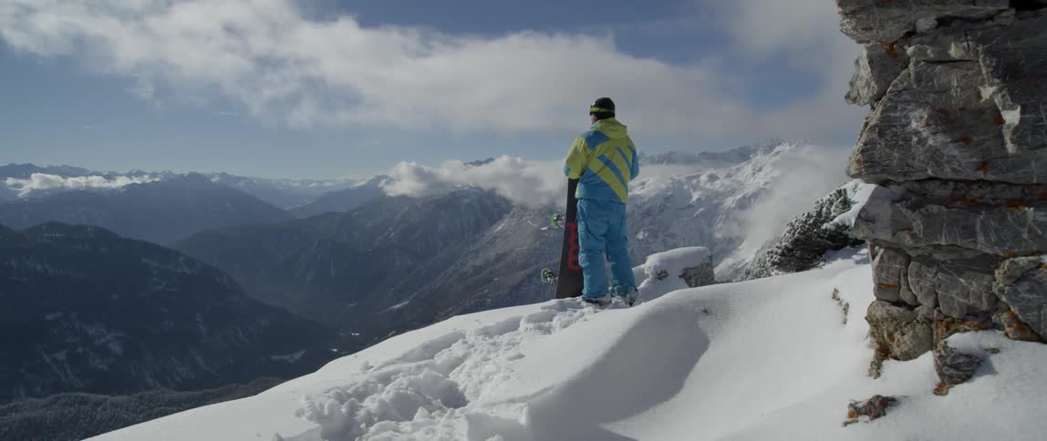 Man stands at the edge of a mountain holding a snowboard