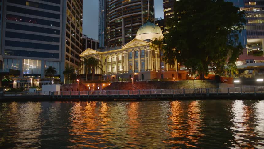 An domed building in a city on a harbor is lit up with lights at dusk