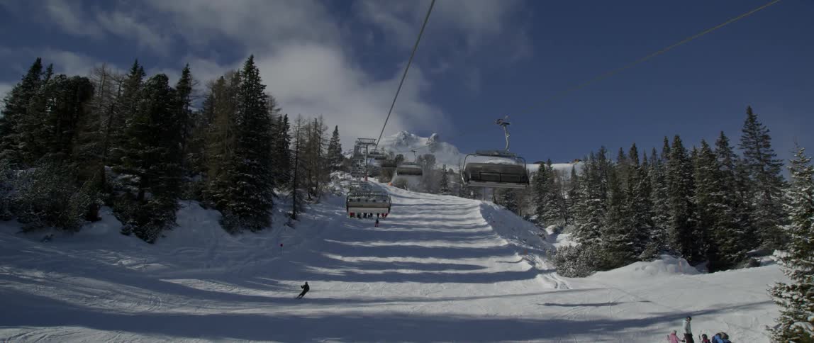 Many people skiing down a hill with a ski lift overhead