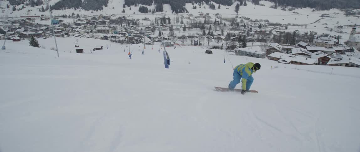 A snowboarder does a 360 as he boards down a mountain in a ski resort
