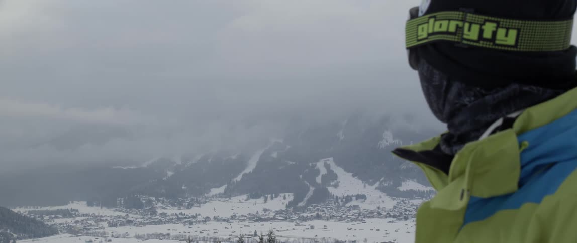 A man in snowboarding gear turns to look at a mountain
