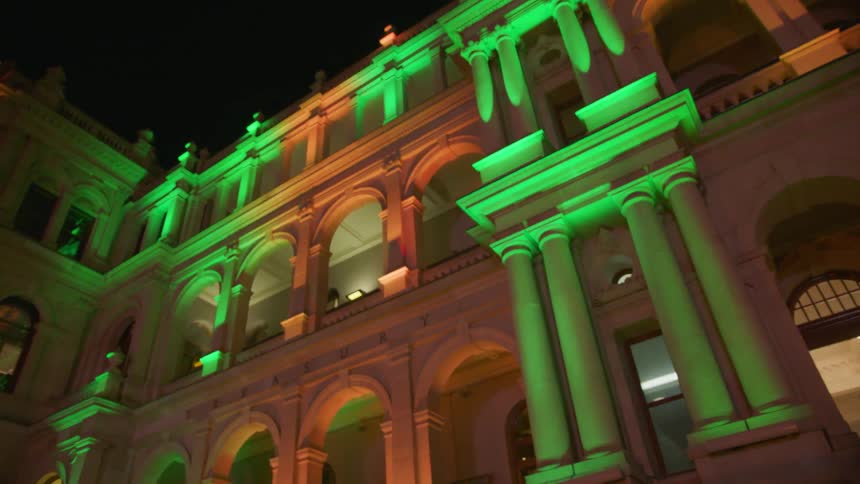 Tourists walk past an old building lit up with colorful lights
