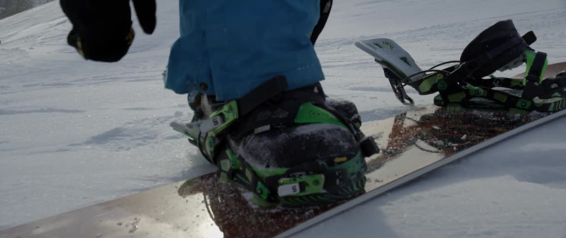 A man steps into the straps of a snowboard