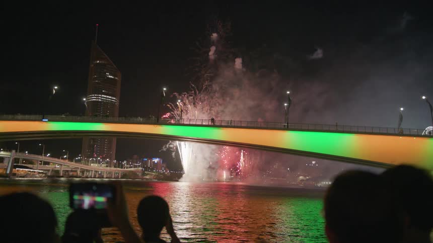 Tourists on a boat take pictures of fireworks on a river at night