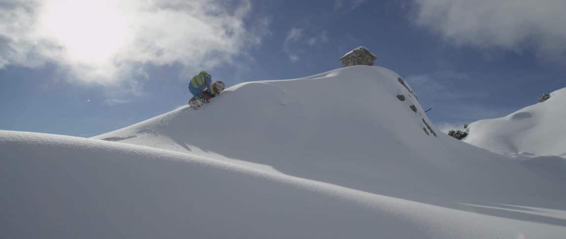 Person carrying a snowboard crawls up a snowy peak