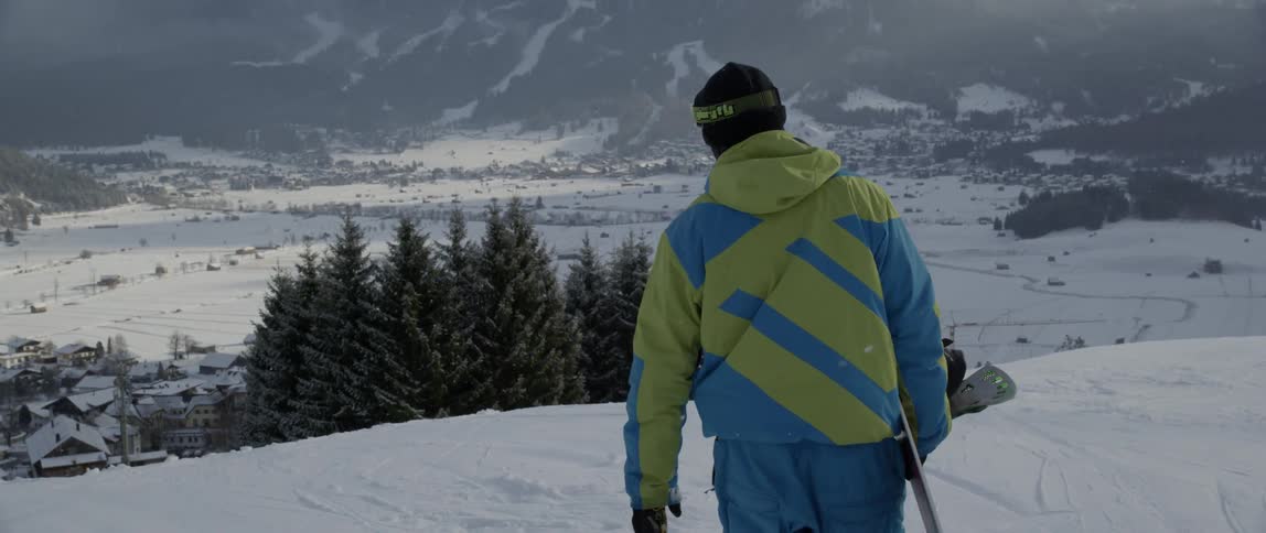 Person carrying a snowboard walks to the edge of a snowy hill