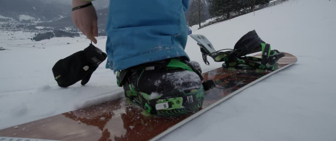 A person straps onto a snowboard