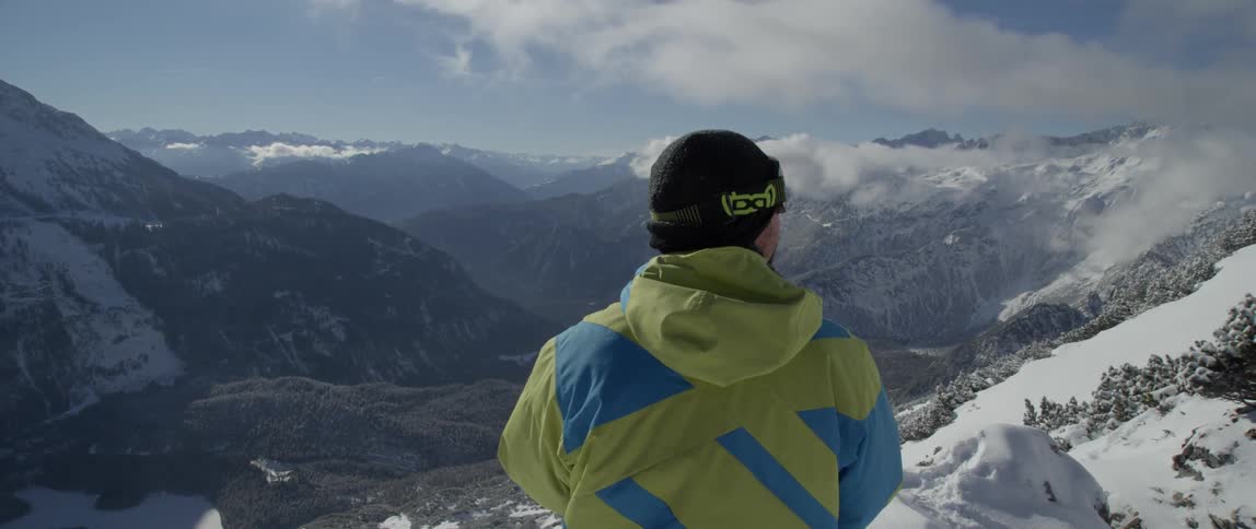 A man stands looking at snow-covered mountains and a valley