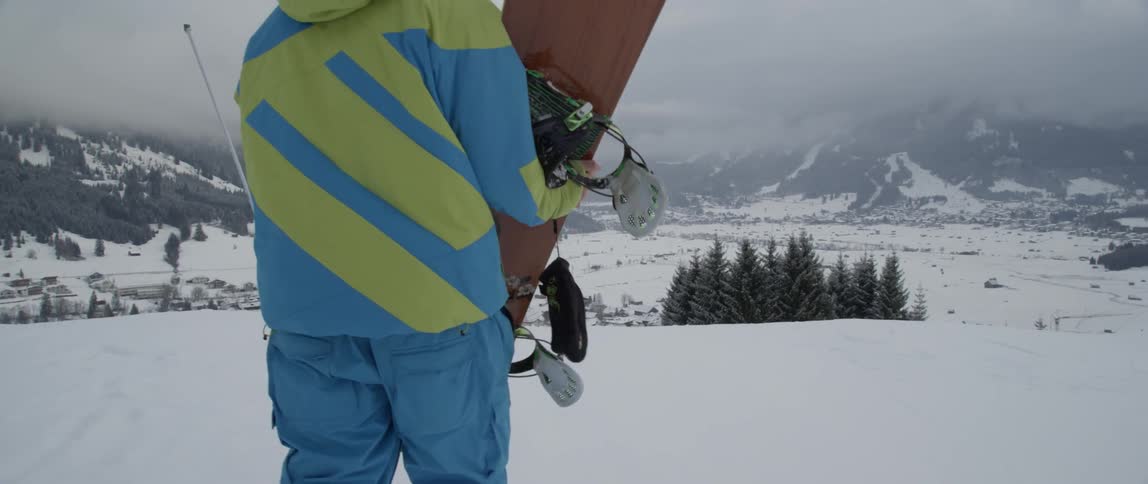 Person carrying a snowboard walking in a snowy field