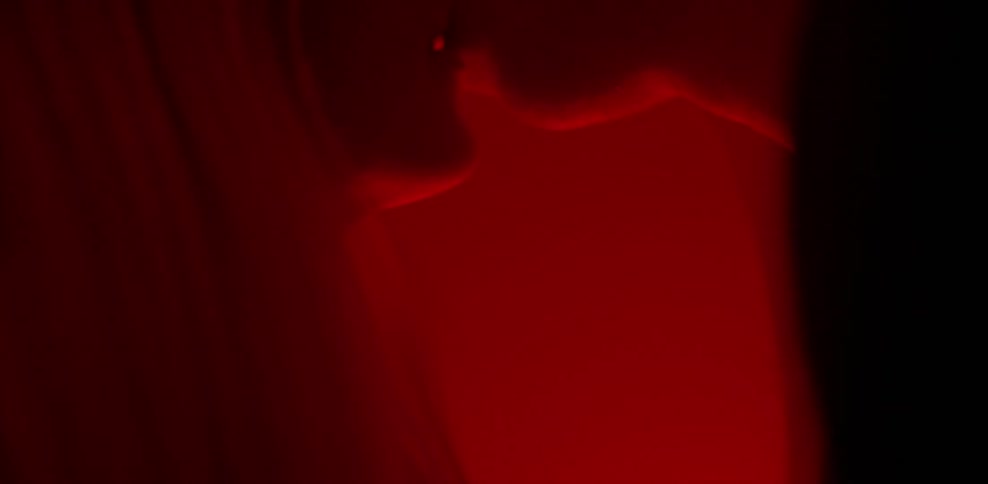 A man and woman kiss with a red light in the background