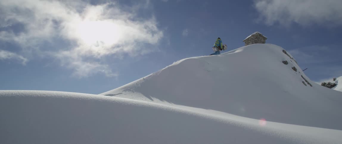 A person carrying a snowboard climbs to the peak