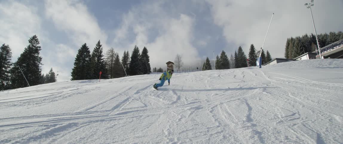 A snowboarder rides down a mountain in a ski resort during the day