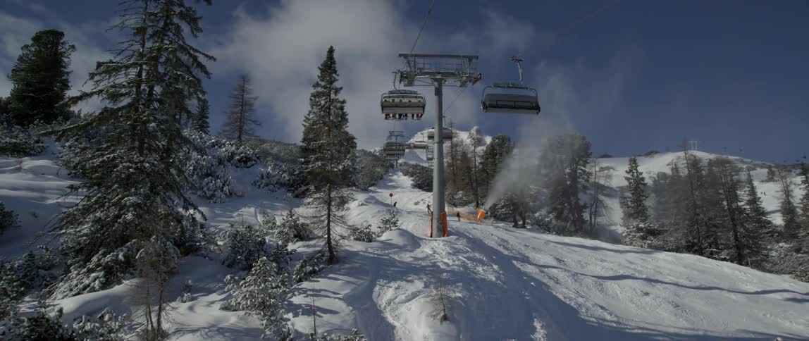 The chair lift goes up the mountain as people ski and board down