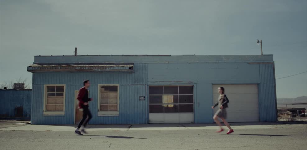 A man and woman run toward each other outside a boarded up building during the day