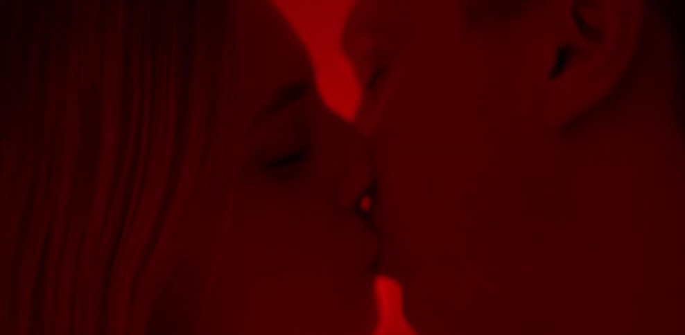 A man and woman are kissing and swaying in a room with red light