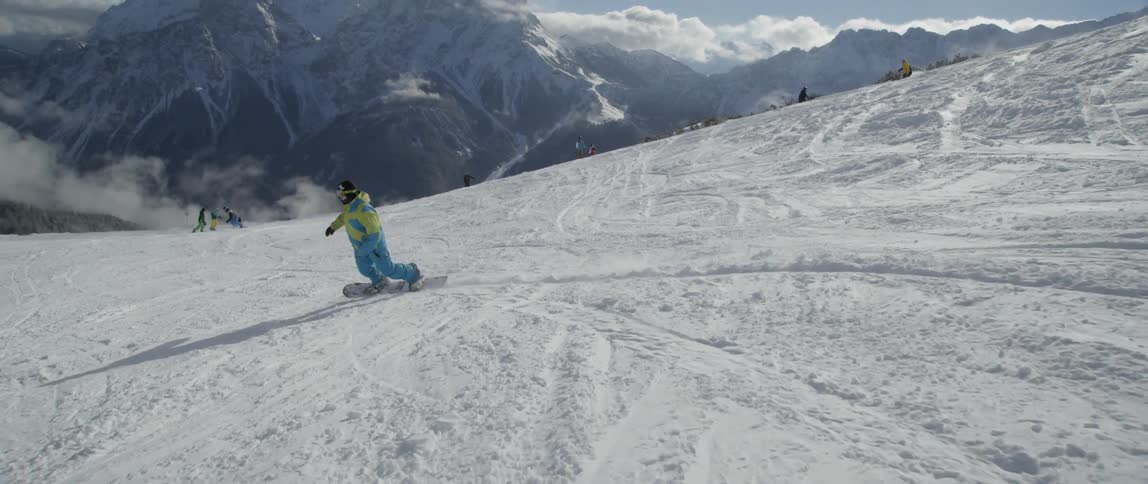 A snowboarder rides down a mountain in a ski resort during the day