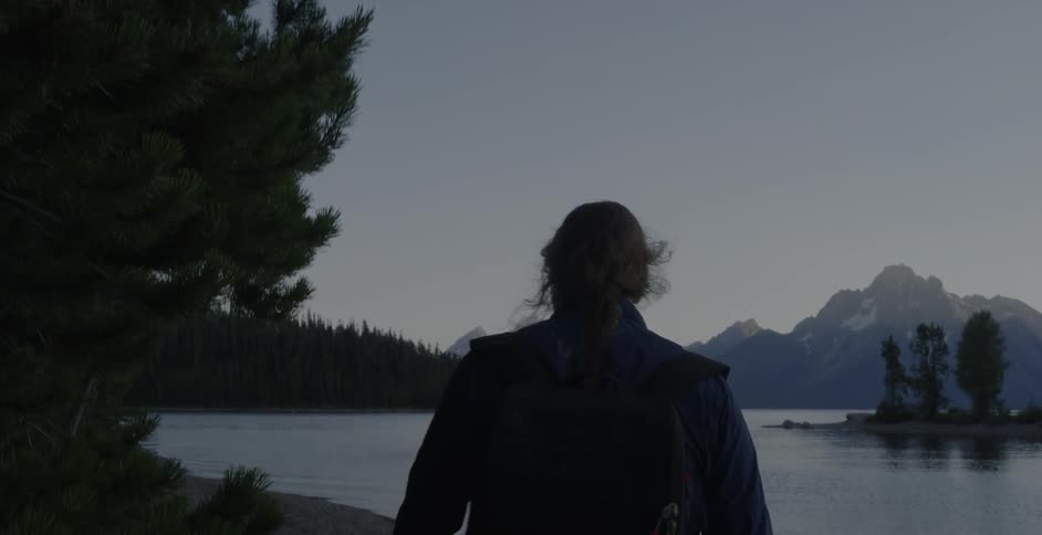 A man puts his hand in his pocket as he walks toward a shoreline at dusk