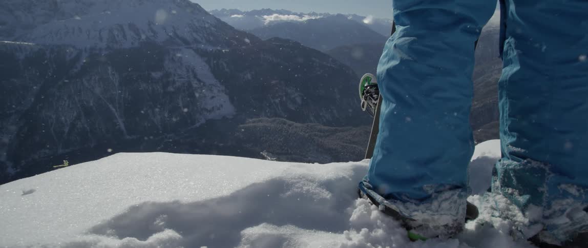Person holding a snowboard stands at the edge of a snowy cliff