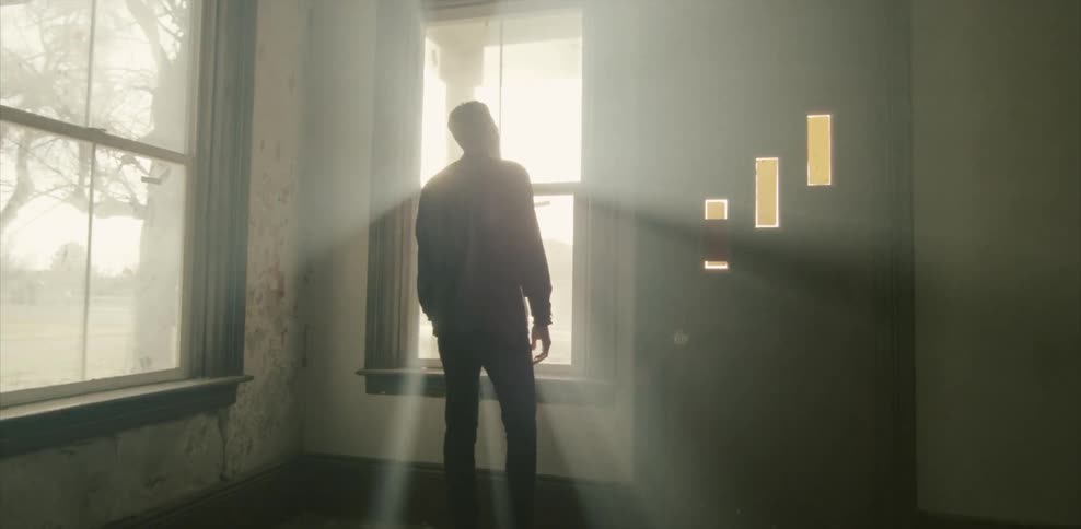 A man stands looking out the window of a vacant, rundown building