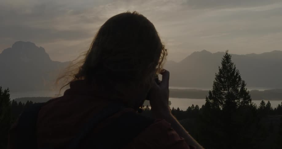 A person takes pictures of a forest and mountain landscape