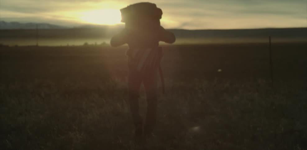 A person wearing a large backpack walks toward the sunset
