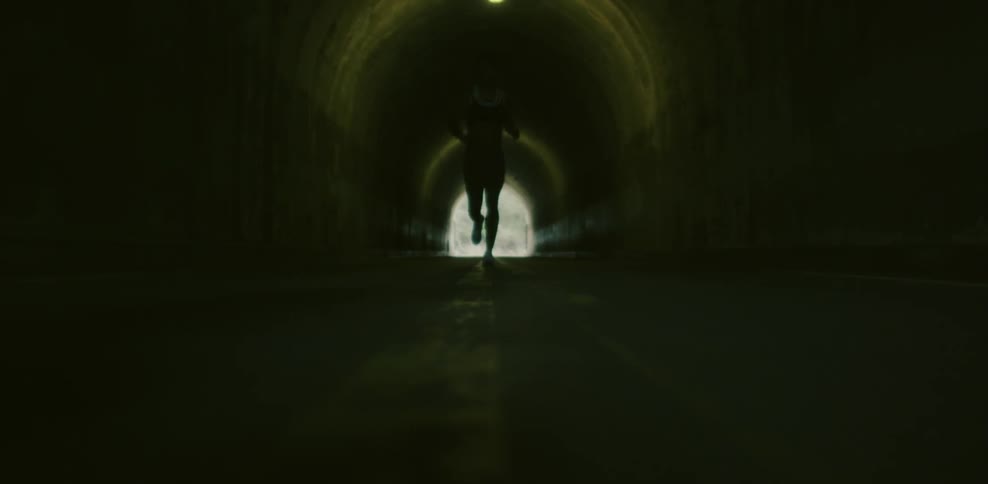 A female jogger is running through a tunnel during the day