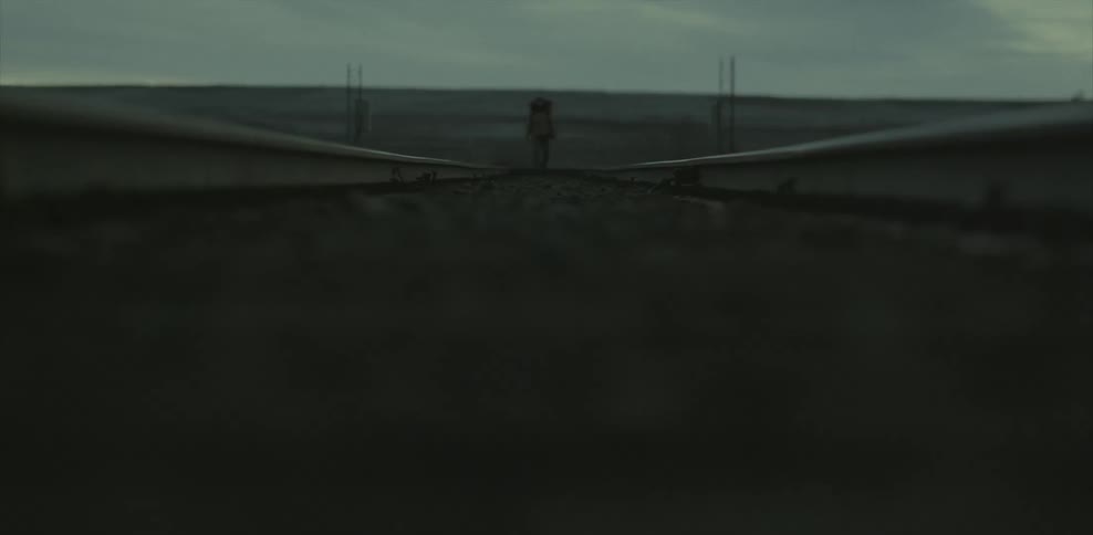A man carrying a heavy backpack is hiking on train rails