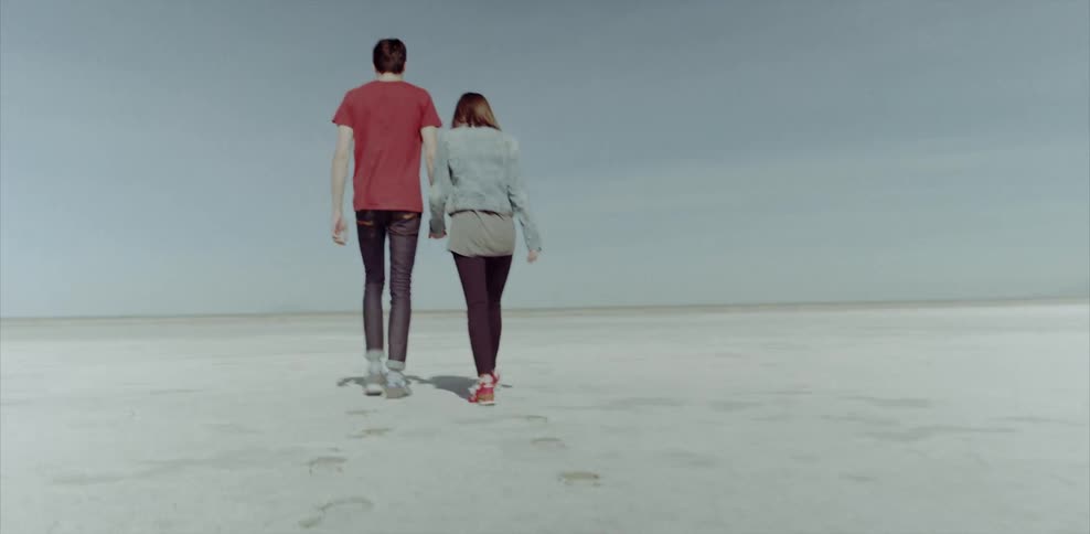 A man and woman hold hands and walk across the sand