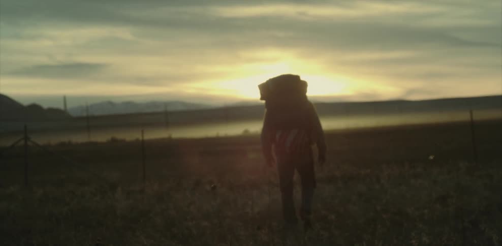 A man wearing a backpack walks across a field