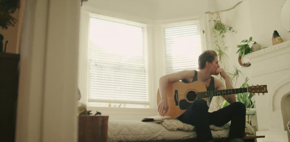 Man sits on a bed holding a guitar