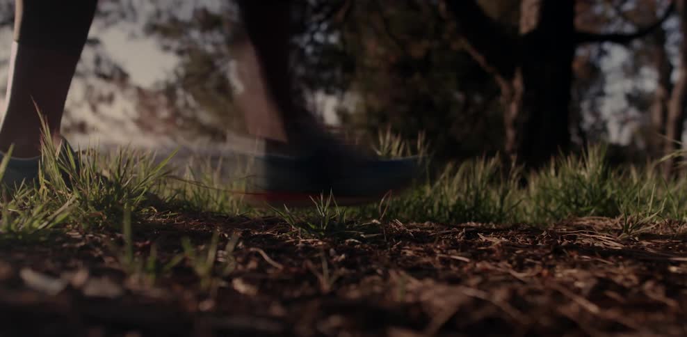 A person walks on a dirt path dotted with clumps of grass