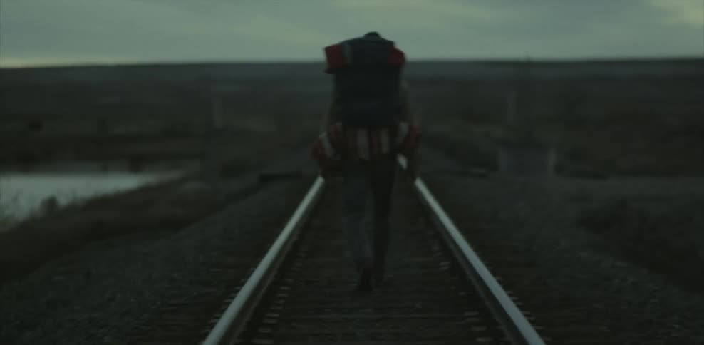 A man wearing a backpack walks up a train track
