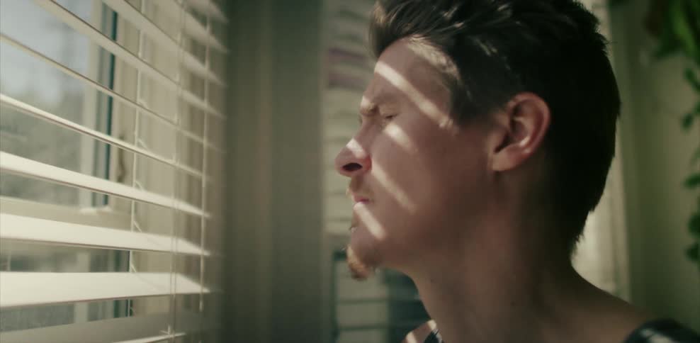 Man looking through window blinds on a sunny day