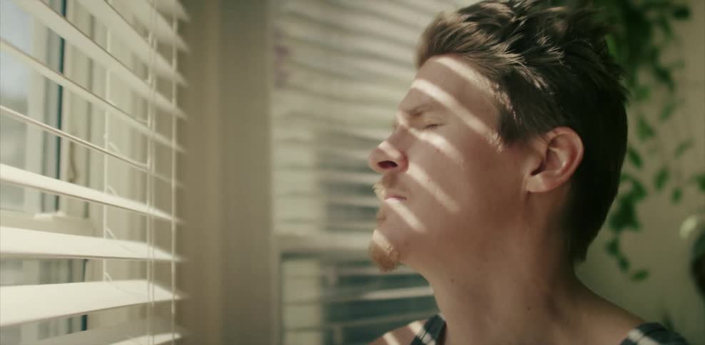 Sunlight shines through blinds onto a man's face