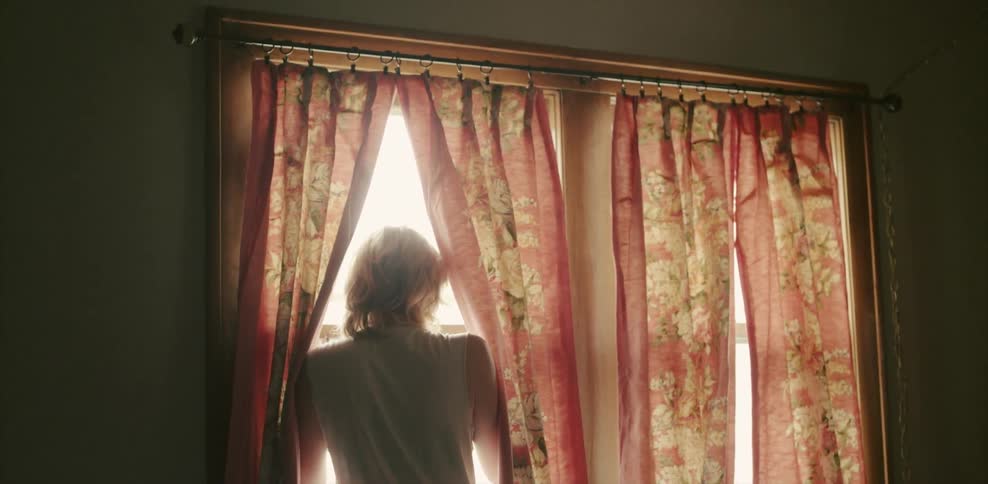 A blonde woman looks out of her window