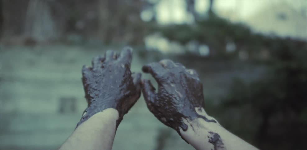 A person rubs their hands in mud