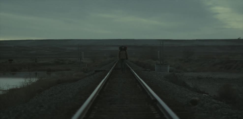 A man carrying a heavy backpack is hiking between the rails on a train track