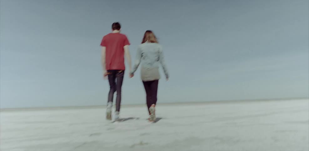 A man and woman hold hands while walking on the sand