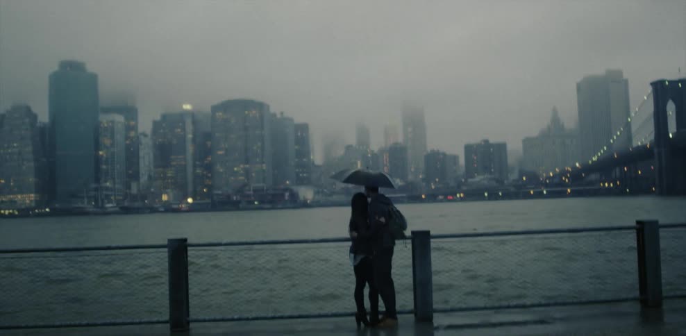 A couple stand under an umbrella near a body of water