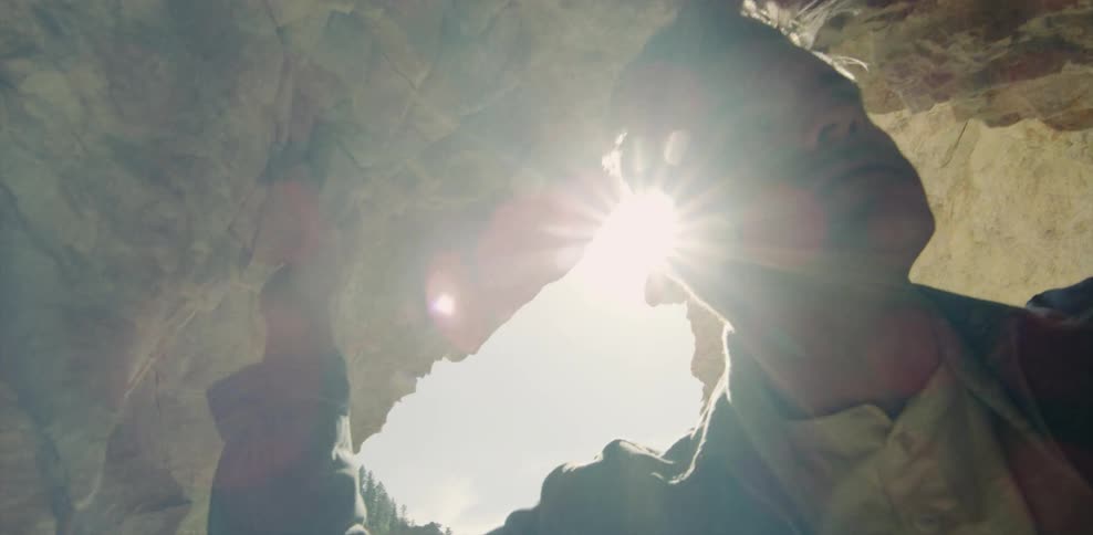 Man stands in a cave looking down on a sunny day