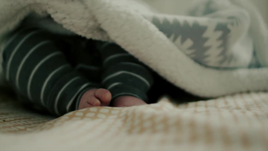 A woman pulls a coverlet over a baby's feet