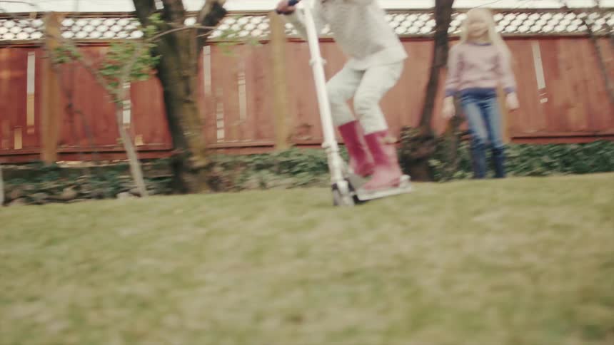 A little girl wearing a big helmet rides a scooter down a hill in a backyard