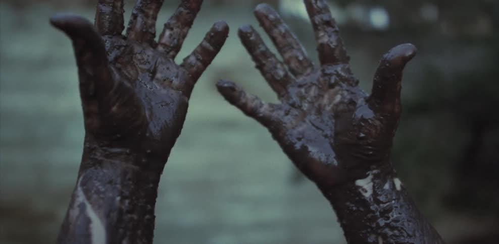 A person is rubbing mud all over their hands and looking at them
