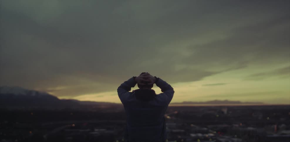 Man standing with hands behind his head looking down at a city